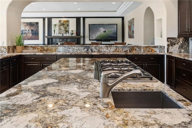 kitchen featuring backsplash, sink, dark brown cabinetry, stainless steel gas cooktop, and stone countertops