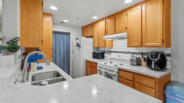 kitchen featuring decorative backsplash, white appliances, light stone counters, and sink