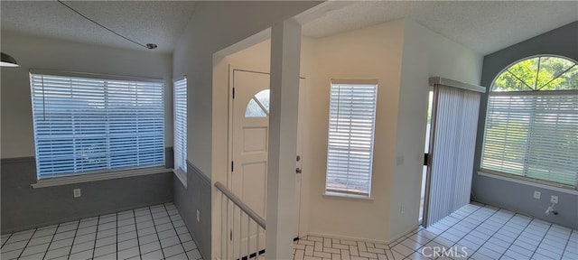 entryway featuring a textured ceiling, lofted ceiling, and light tile patterned floors