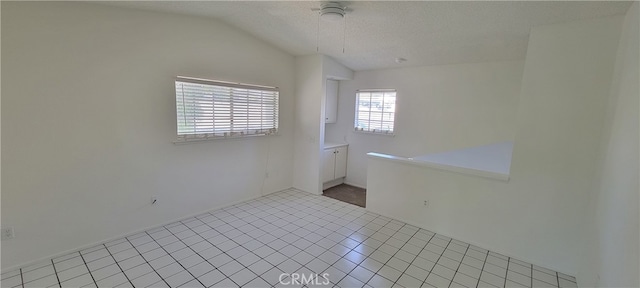 unfurnished room with a textured ceiling, lofted ceiling, light tile patterned flooring, and ceiling fan