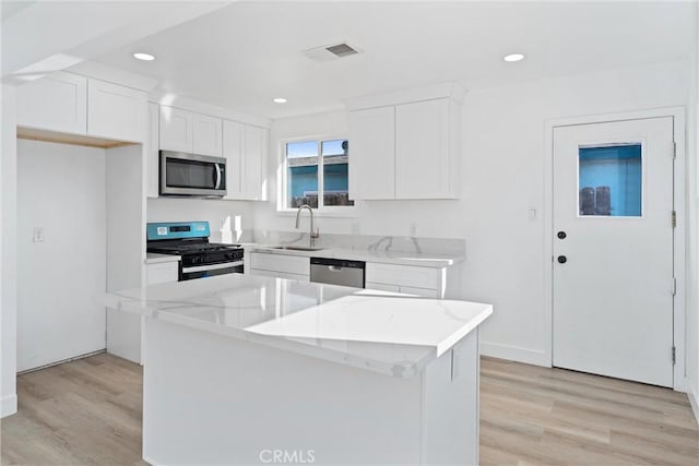 kitchen with appliances with stainless steel finishes, light wood-type flooring, sink, white cabinets, and a center island