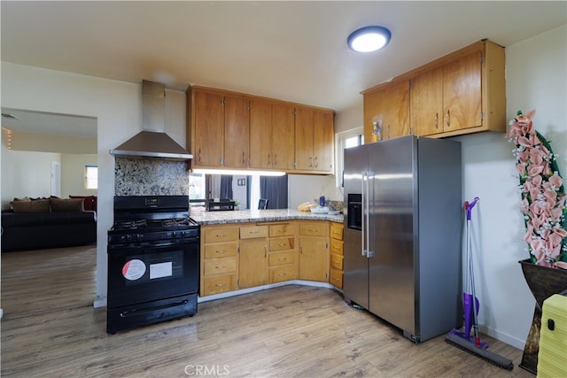 kitchen featuring black gas stove, light wood-type flooring, stainless steel fridge with ice dispenser, tasteful backsplash, and wall chimney exhaust hood