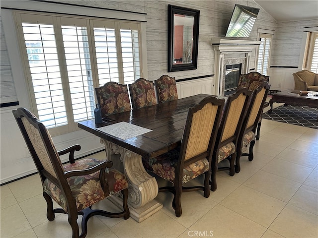 dining room with wood walls, light tile patterned floors, vaulted ceiling, and a healthy amount of sunlight