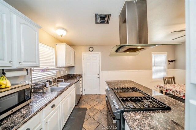 kitchen featuring sink, stainless steel appliances, island exhaust hood, dark stone countertops, and white cabinets