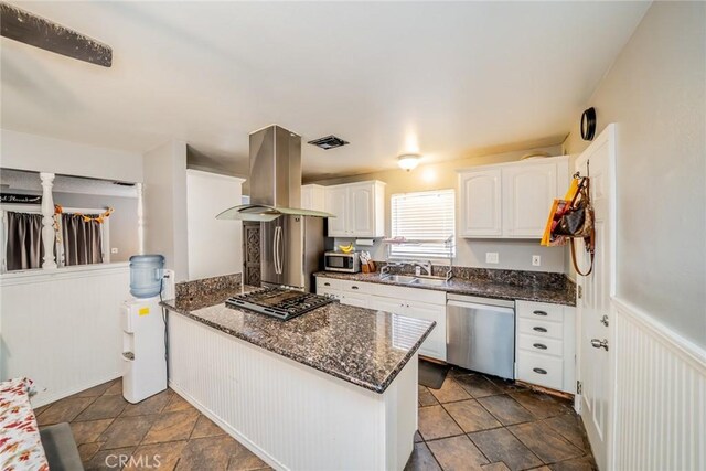 kitchen with sink, stainless steel appliances, island exhaust hood, dark stone counters, and white cabinets