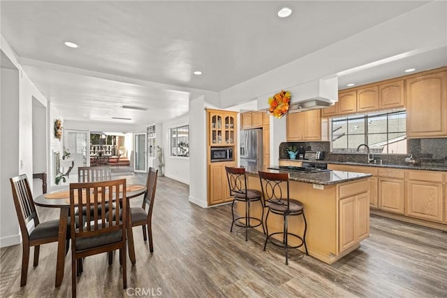 kitchen featuring tasteful backsplash, hardwood / wood-style floors, dark stone counters, a kitchen island, and appliances with stainless steel finishes