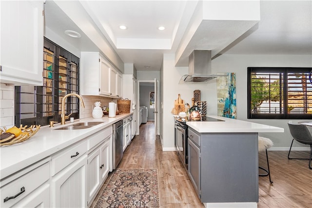 kitchen featuring a breakfast bar area, sink, wall chimney range hood, and white cabinets