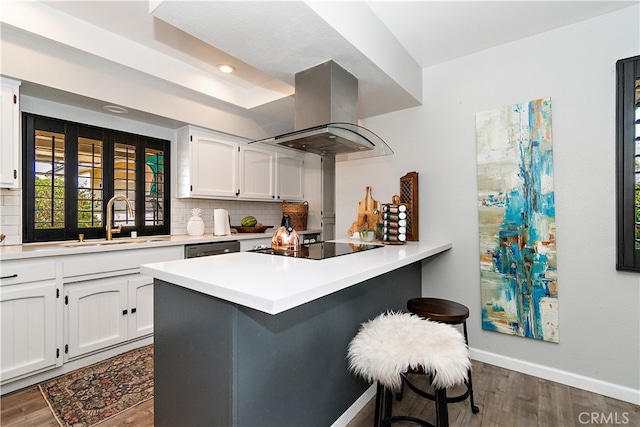 kitchen featuring a breakfast bar, white cabinetry, kitchen peninsula, and range hood