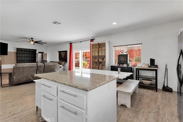 kitchen with white cabinets, ceiling fan, a kitchen island, and light hardwood / wood-style flooring