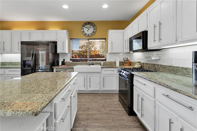 kitchen with sink, light stone counters, hardwood / wood-style floors, white cabinets, and black appliances