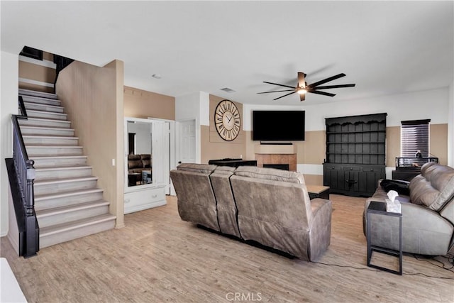 living room with a tile fireplace, ceiling fan, and light hardwood / wood-style floors