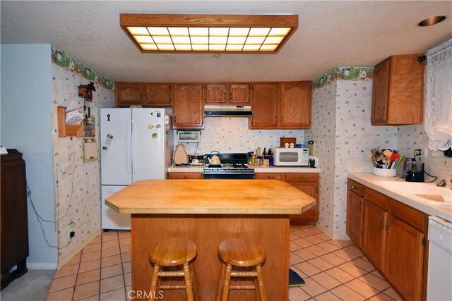 kitchen featuring wallpapered walls, white appliances, light tile patterned floors, and under cabinet range hood