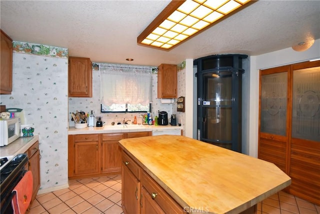 kitchen featuring white microwave, wooden counters, wallpapered walls, light tile patterned flooring, and range