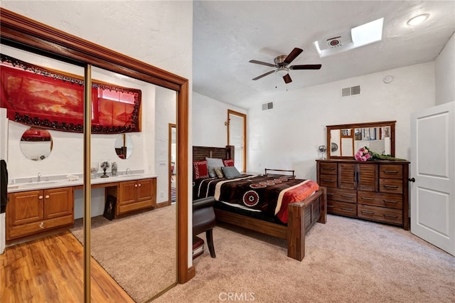 bedroom with sink, light wood-type flooring, built in desk, a textured ceiling, and ceiling fan