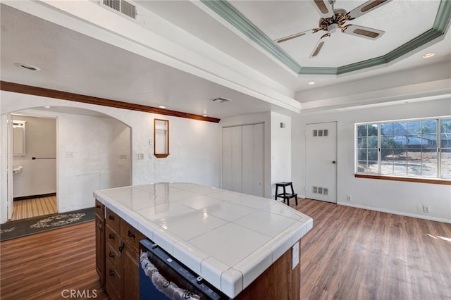 kitchen with ornamental molding, dark wood-type flooring, tile counters, dark brown cabinetry, and a center island