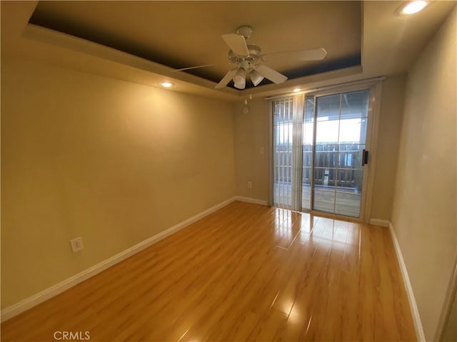 empty room with light wood-type flooring, a tray ceiling, and ceiling fan