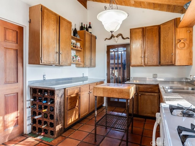 kitchen featuring gas range gas stove, sink, hanging light fixtures, vaulted ceiling with beams, and stainless steel counters