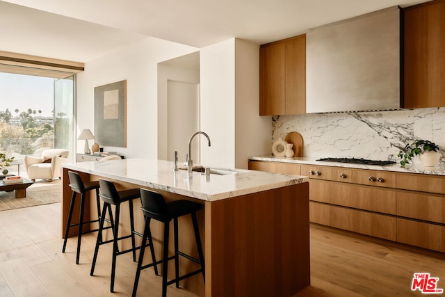 kitchen with sink, tasteful backsplash, a center island with sink, gas cooktop, and light wood-type flooring