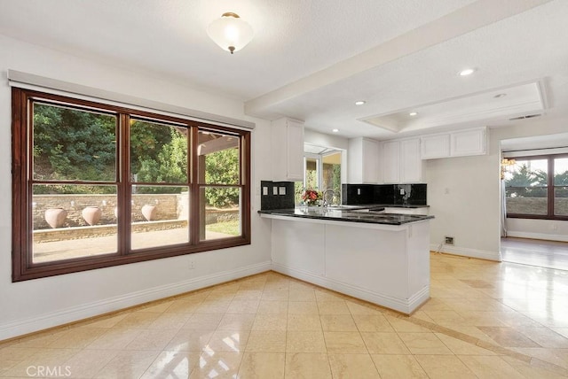 kitchen with a raised ceiling, kitchen peninsula, decorative backsplash, light tile patterned flooring, and white cabinetry