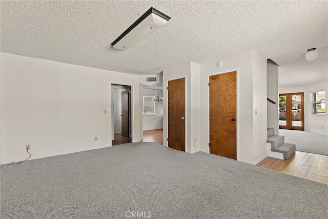 unfurnished bedroom with french doors, a textured ceiling, ensuite bath, and light colored carpet