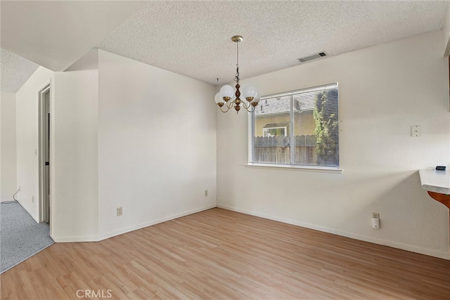 empty room with light hardwood / wood-style flooring, a textured ceiling, and a notable chandelier