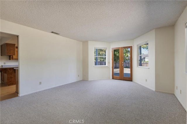 carpeted empty room with french doors, a textured ceiling, and plenty of natural light