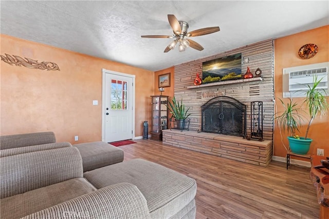 living room with hardwood / wood-style floors, a large fireplace, a textured ceiling, a wall unit AC, and ceiling fan