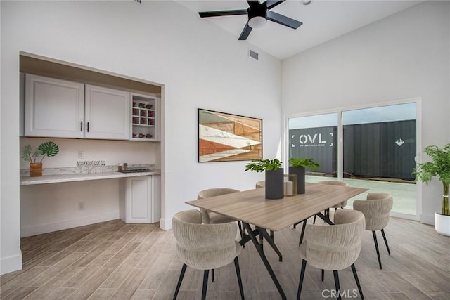 dining room with ceiling fan, visible vents, baseboards, built in study area, and light wood finished floors