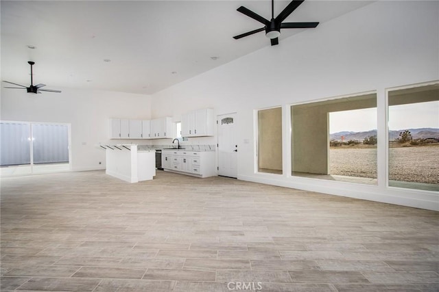 unfurnished living room with high vaulted ceiling, a mountain view, light hardwood / wood-style flooring, ceiling fan, and sink