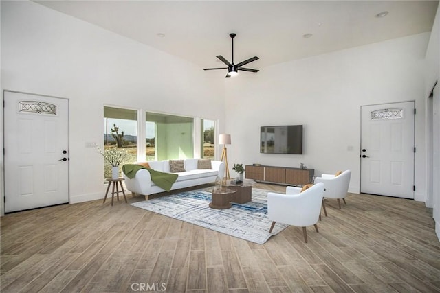 living area featuring ceiling fan, a high ceiling, baseboards, and wood finished floors