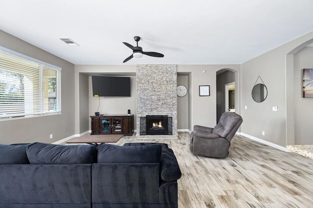 living room featuring ceiling fan, a stone fireplace, and light hardwood / wood-style floors