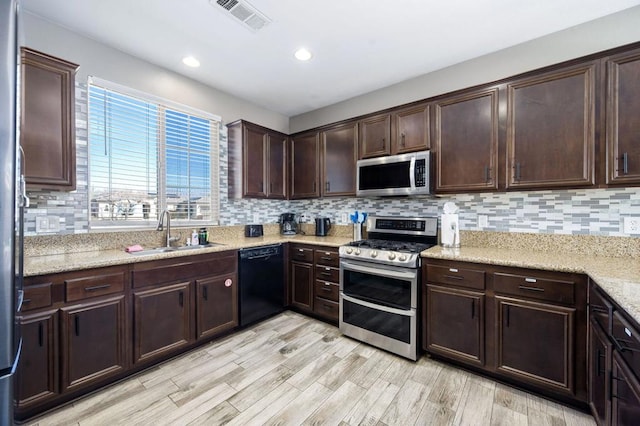 kitchen featuring appliances with stainless steel finishes, backsplash, light wood-type flooring, dark brown cabinetry, and sink