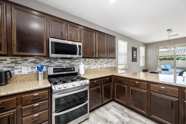 kitchen with dark brown cabinetry, hanging light fixtures, tasteful backsplash, stainless steel appliances, and light hardwood / wood-style floors