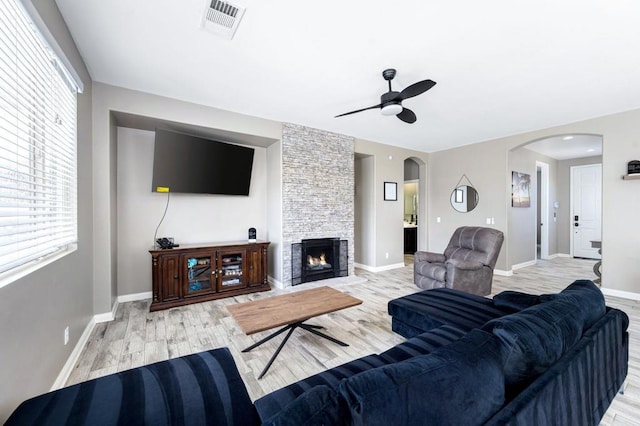 living room featuring ceiling fan, a stone fireplace, and light wood-type flooring