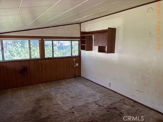 carpeted spare room featuring wooden walls and lofted ceiling