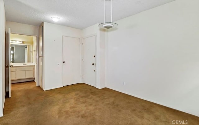 unfurnished bedroom with ensuite bath, a textured ceiling, and carpet floors