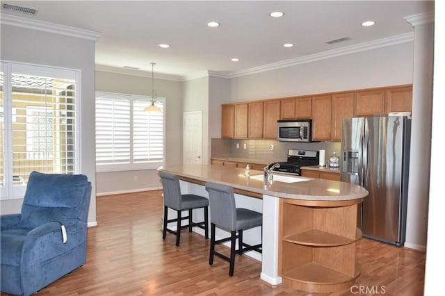 kitchen featuring an island with sink, light wood-type flooring, decorative light fixtures, appliances with stainless steel finishes, and ornamental molding