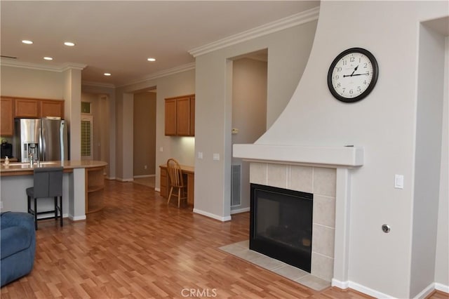 living room with a tile fireplace, light hardwood / wood-style floors, and ornamental molding