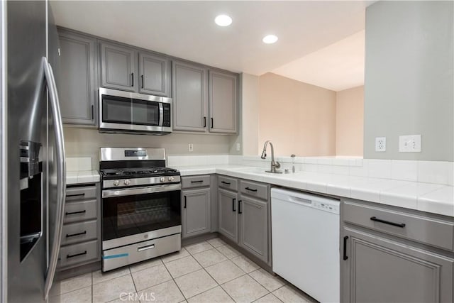 kitchen featuring appliances with stainless steel finishes, gray cabinetry, sink, light tile patterned floors, and tile counters