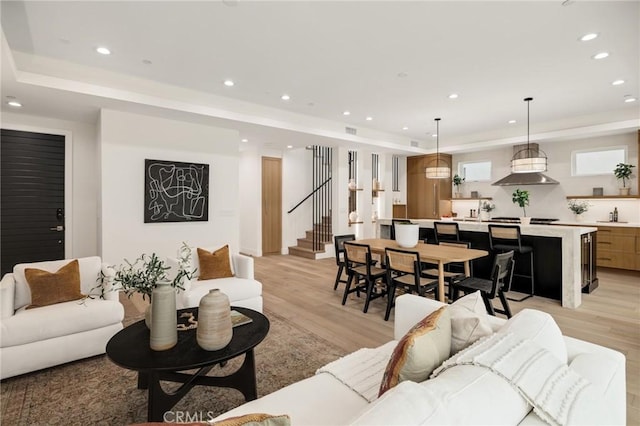 living area with a tray ceiling, stairway, light wood-style flooring, and recessed lighting