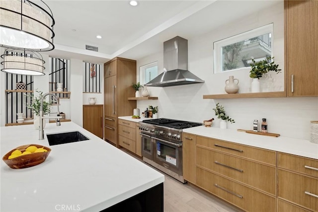 kitchen featuring recessed lighting, a sink, light countertops, wall chimney range hood, and double oven range