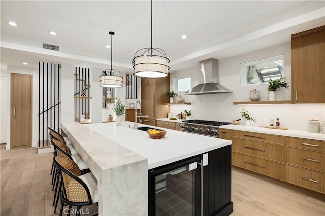 kitchen featuring light wood finished floors, light countertops, a sink, wall chimney range hood, and beverage cooler