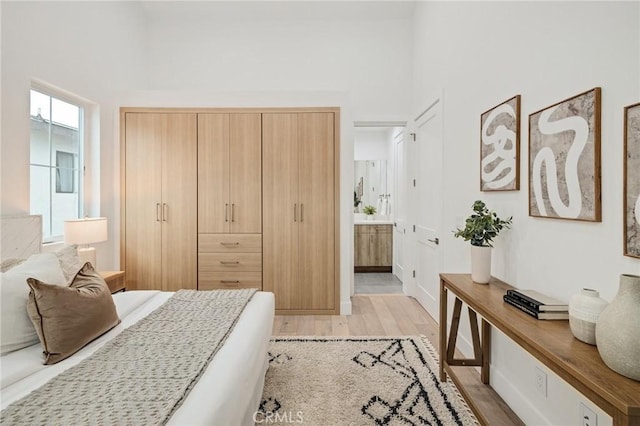 bedroom with light wood-style floors, a towering ceiling, and ensuite bath