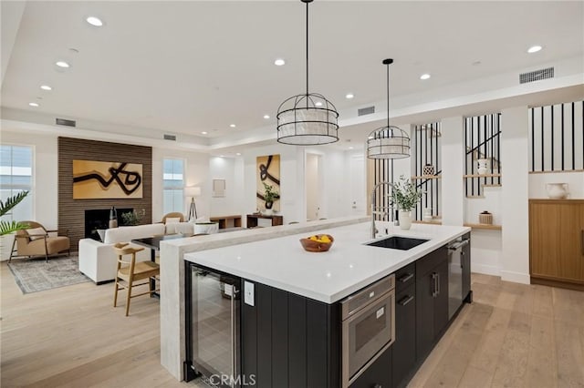 kitchen with wine cooler, a fireplace, light wood-style flooring, a sink, and dark cabinetry