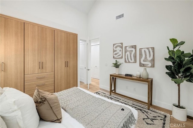 bedroom featuring light wood-type flooring, high vaulted ceiling, baseboards, and visible vents