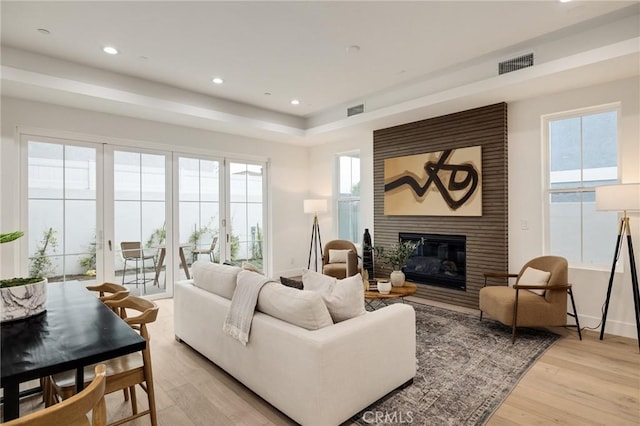 living room with a healthy amount of sunlight, a large fireplace, light wood-style flooring, and visible vents