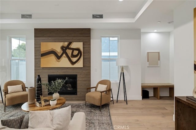 living area featuring light wood-type flooring, a wealth of natural light, a fireplace, and visible vents