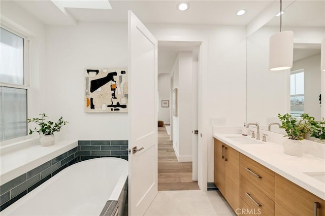 bathroom with double vanity, wood finished floors, a freestanding bath, a sink, and recessed lighting