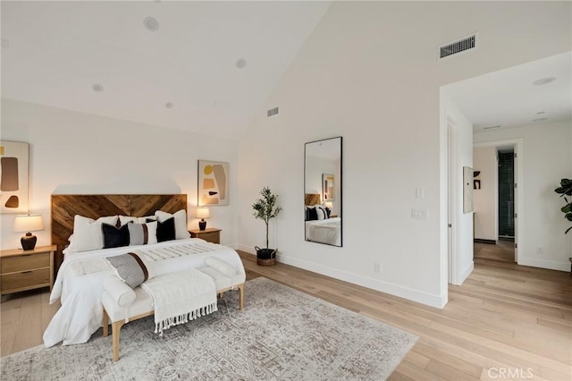 bedroom featuring light wood finished floors, baseboards, visible vents, and high vaulted ceiling