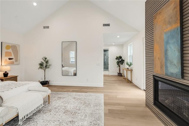 bedroom featuring a large fireplace, high vaulted ceiling, light wood finished floors, and visible vents